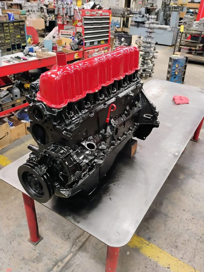 A finished inline six, painted and assembled, on the bench with racked crankshafts behind it