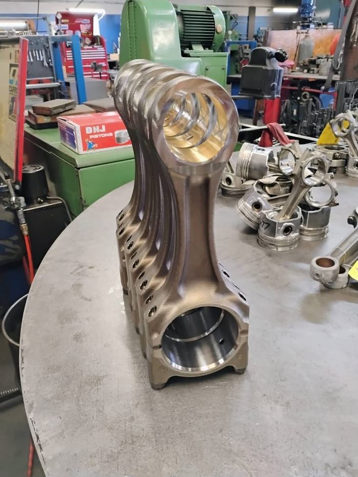 A reconditioned connecting rod standing on the bench at RPM Machine, with more rods and pistons laid out behind it