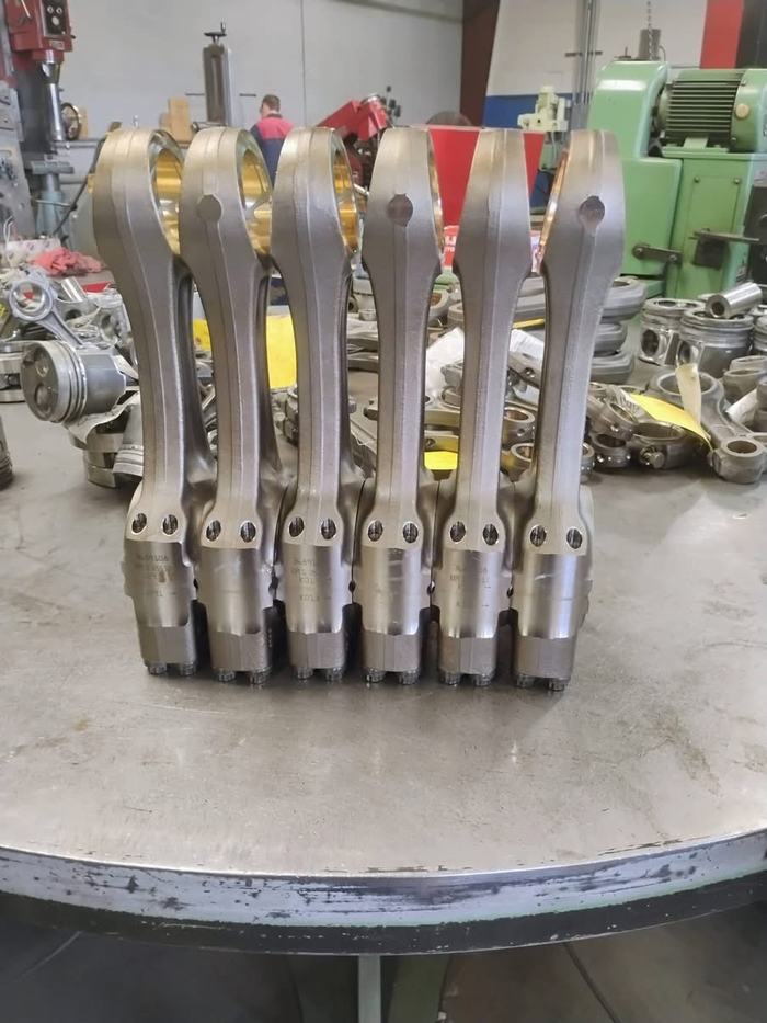 Six matched connecting rods lined up across the bench after reconditioning